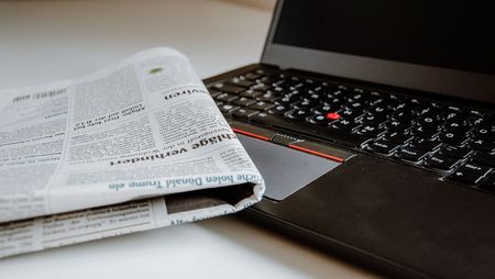 Eine Zeitung liegt halb auf der Tastatur eines Laptops.