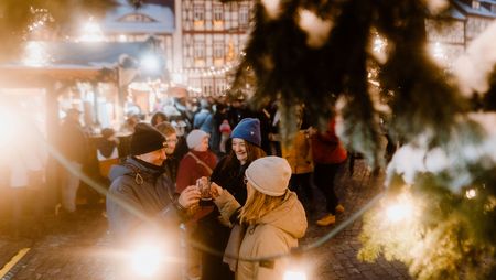 Eine Personengruppe steht zum Weihnachtsmarkt auf dem Marktplatz in Wernigerode unter dem Weihnachtsbaum und trinkt Glühwein.