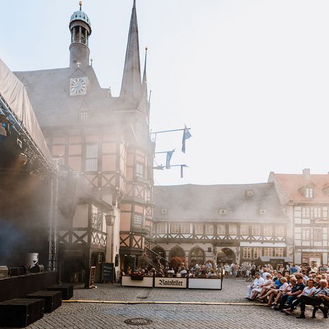 Publikum sitzt auf Bänken vor einer Bühne auf dem Marktplatz zum Rathausfest in Wernigerode.