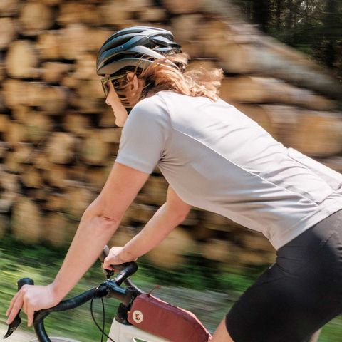 Eine Teilnehmerin am Gravel Bike Fest in Schierke fährt auf dem Fahrrad an einem Holzstapel vorbei.