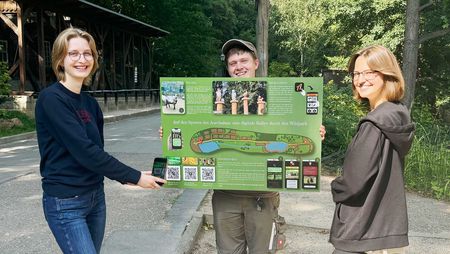 Drei Personen halten ein Schild hoch auf dem es Hinweise zur Rallye durch den Wildpark Christianental in Wernigerode gibt.