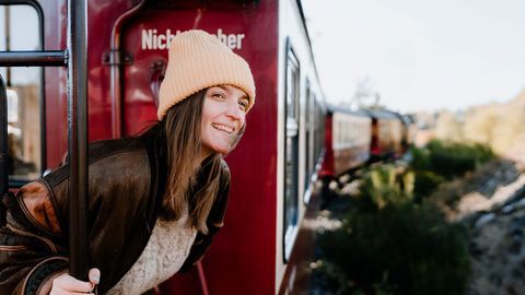 Eine Frau steht auf einer Außenplattform der Harzer Schmalspurbahn und schaut aus der fahren Bahn.