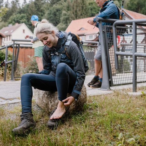 Eine Person sitzt während der 24h-Wandertrophy auf einem Stein und hat sich einen Schuh ausgezogen.
