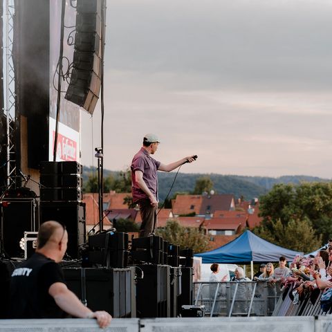 Ein Sänger steht auf der Bühne des MDR Harz Open Airs in Wernigerode. Vor Ihm das Publikum und hinter ihm sind die Berge des Harzes zu erkennen.